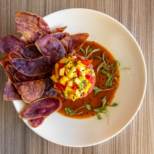 Tuna tartare with mango salsa, purple sweet potato chips, and a savory sauce on a white plate.