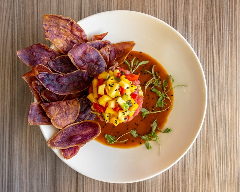 Tuna tartare with mango salsa, purple sweet potato chips, and a savory sauce on a white plate.