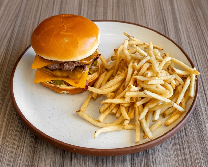 A cheeseburger with two patties and a side of golden french fries on a white plate.