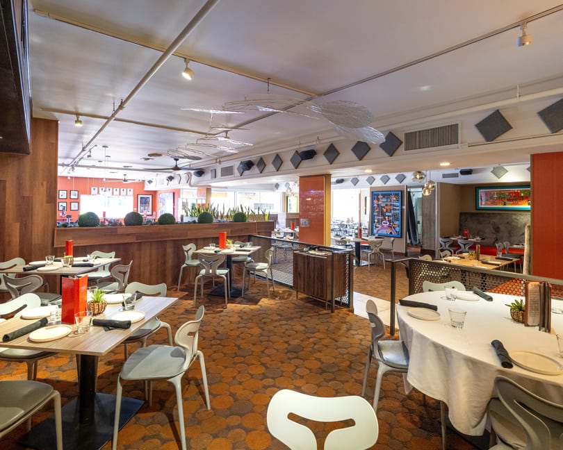 A spacious, modern restaurant dining room with set tables, patterned carpet, and contemporary decor.