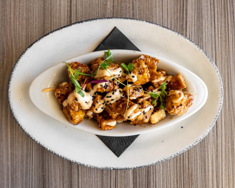 Crispy fried chicken bites drizzled with creamy sauce, black sesame seeds, and fresh herbs.