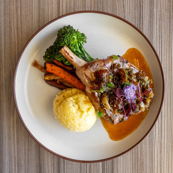 Pork chop with mashed potatoes, roasted carrots, broccolini, and a rich sauce on a white plate.