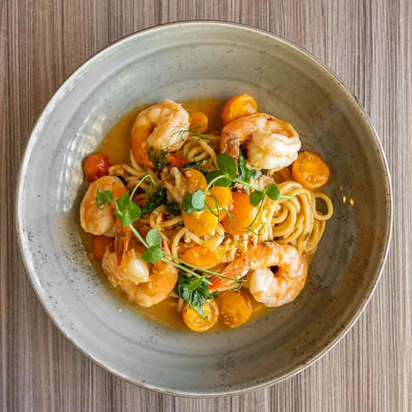 Shrimp scampi pasta with cherry tomatoes and fresh herbs in a gray bowl on a wooden table.