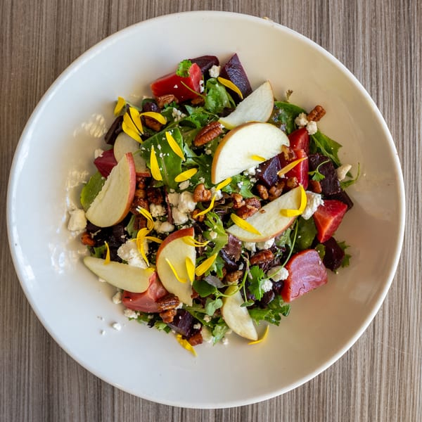 Overhead view of a vibrant salad with mixed greens, beets, apples, pecans, feta, and yellow petals.